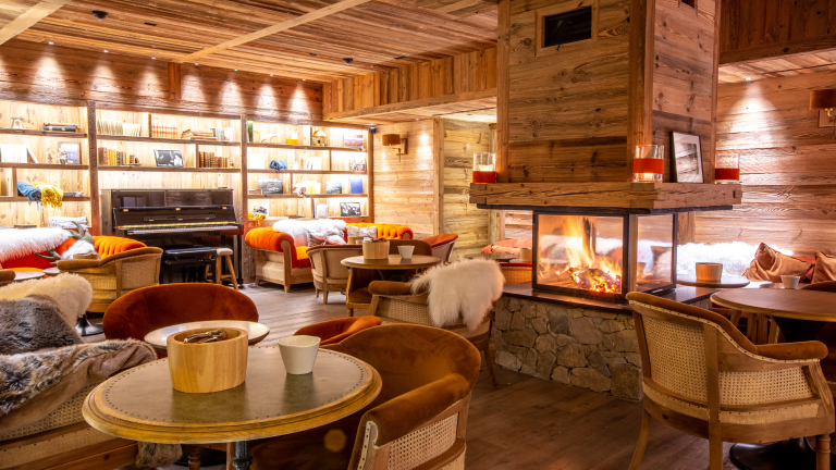 Ambiance cocooning au salon avec chemine centrale, plaid en peau de bte et plafond et mur en bois.