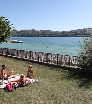 vue sur la plage du pin partie herbore avec une famille prenant un bain de soleil sur leurs serviettes, grand ciel bleu et vue sur le lac de paladru