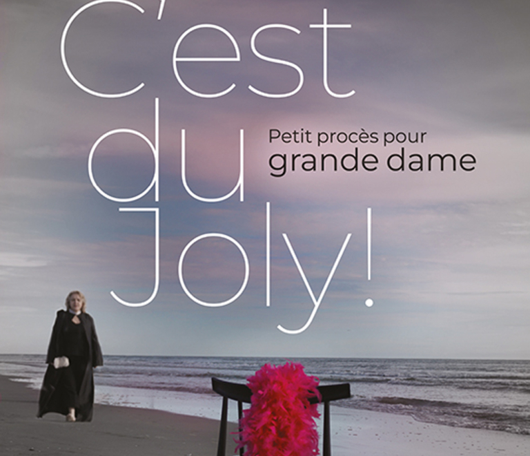 Femme marchant sur la plage en arrire plan avec un boa rouge pos sur une chaise en premier plan. Les couleurs sont sombre et le nom de la pice "C'est du Joly" est inscrit en grand accompagn de la phrase "petit procs pour grande dame".